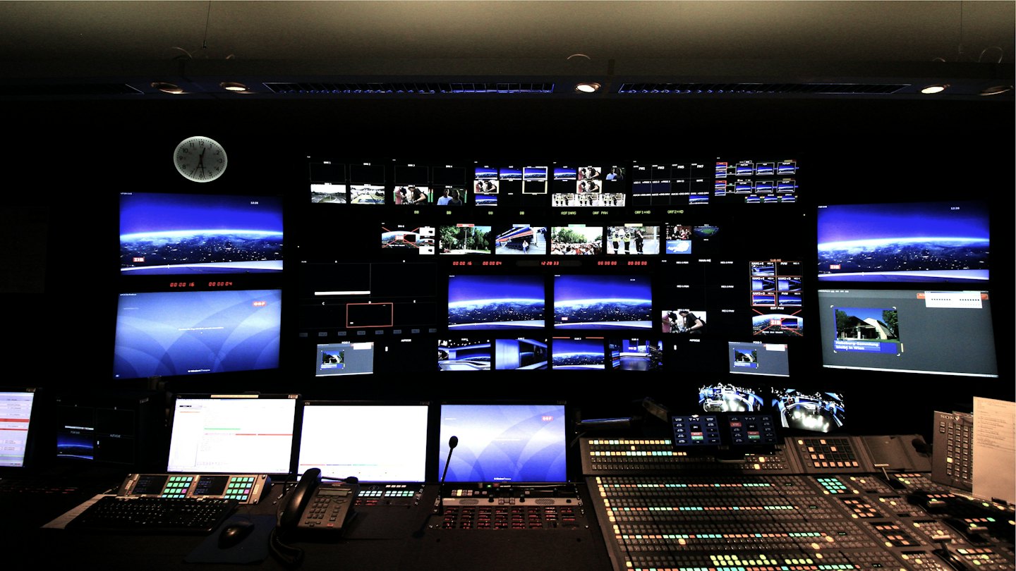 Sala di controllo di trasmissione con monitor luminosi e pannelli di controllo.